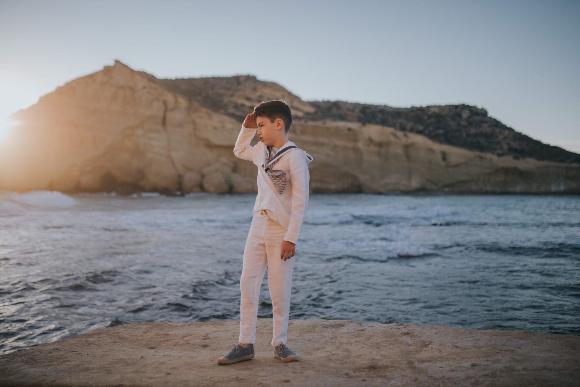 Niño en la playa observando el horizonte con traje de comunión