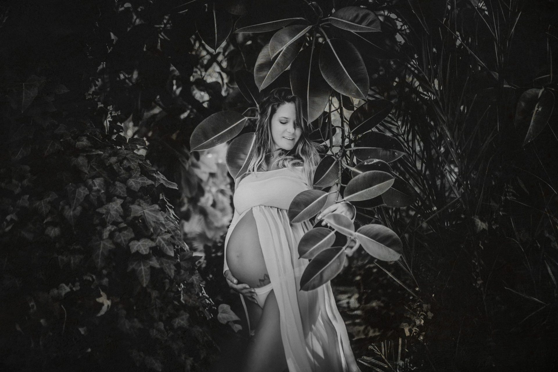 Fotografía en blanco y negro de una mujer embarazada entre plantas del bosque