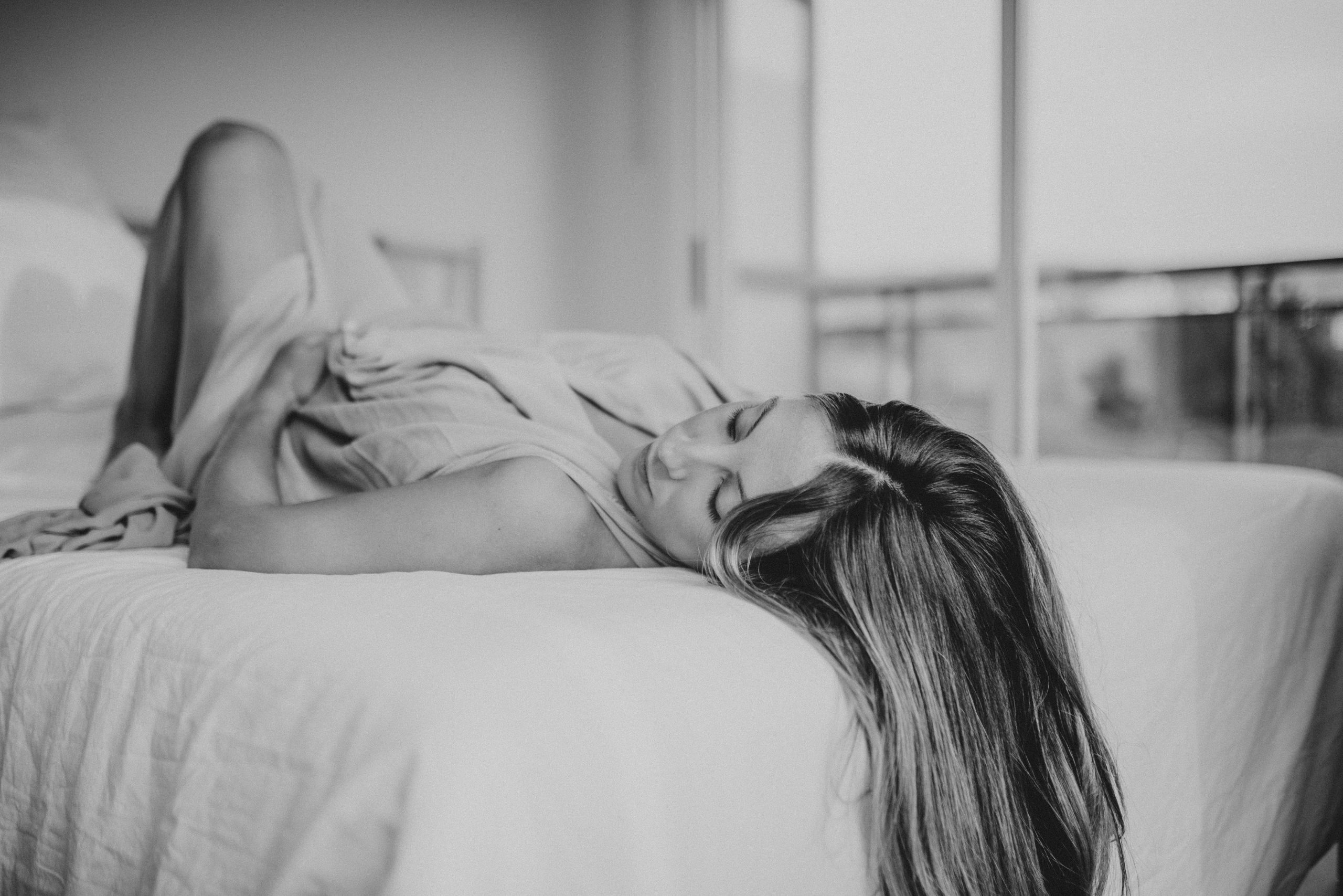 Fotografía en blanco y negro de una mujer sobre una cama acariciando su barriga de embarazada