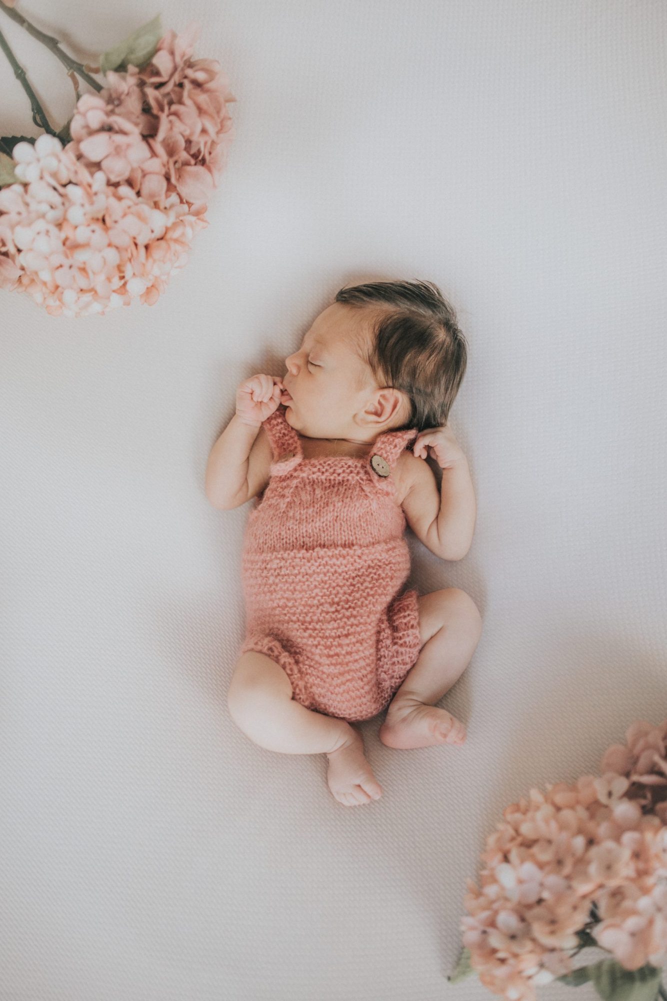 Bebé acostado sobre sábana blanca con flores rosadas